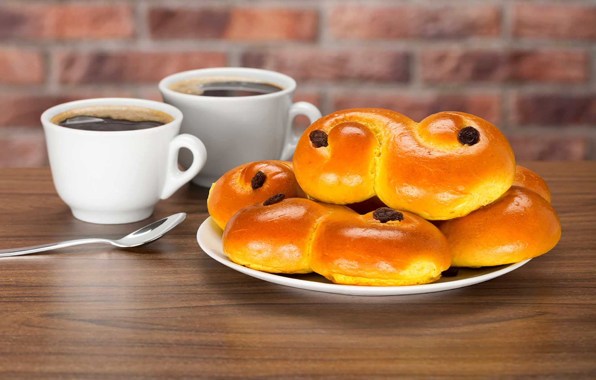 Ett bord med två koppar kaffe och lussebullar på en tallrik, foto.